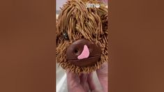 a stuffed animal made out of straw with pink nose and brown hair is being held up by someone's hand