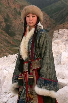 a woman standing on top of a snow covered slope wearing a fur hat and coat