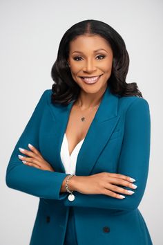 a woman in a blue jacket and white shirt is posing for a photo with her arms crossed