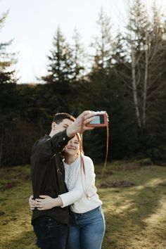 a man and woman taking a photo with their cell phone while standing in the grass