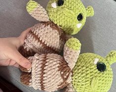 two small stuffed animals sitting next to each other on a couch in front of a person's hand