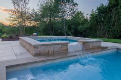 an outdoor swimming pool surrounded by stone steps and water features, with trees in the background