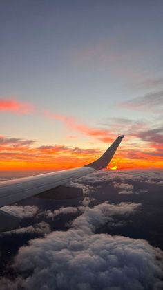 the wing of an airplane as it flies through the sky at sunset with clouds below