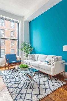 a living room with blue walls and white furniture in front of a large glass window