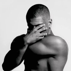 a shirtless man covers his face with his hands while standing in front of a white background