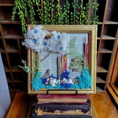 an old book with plants and rocks in it on a table next to a bookshelf