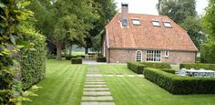 a house that is sitting in the grass next to some bushes and trees with chairs on it