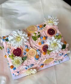 a pink cake decorated with fruit and flowers on top of a white tablecloth covered bed