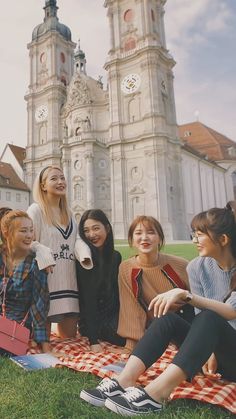 group of young women sitting on the grass in front of a building with two towers