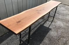 a long wooden table sitting on top of a metal stand next to a gray wall