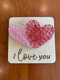 two red and pink paper hearts sitting on top of a white card that says i love you