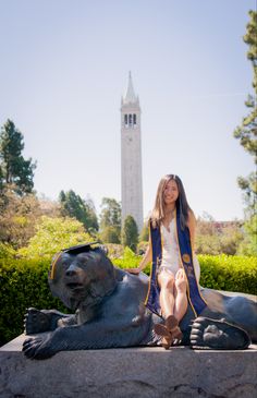 a woman sitting on top of a lion statue in front of a tall building with a clock tower behind her