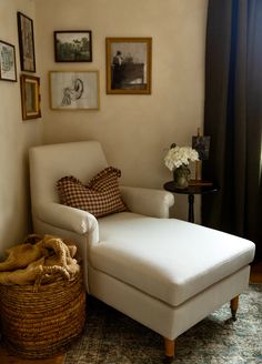 a white chair and ottoman in a room with pictures on the wall above it, along with a basket full of flowers