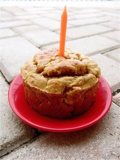 a cupcake sitting on top of a red plate with a candle sticking out of it