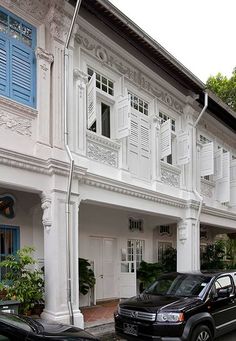 two cars are parked in front of a white building with blue shutters on the windows