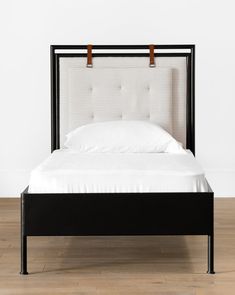 a black bed frame with white sheets and pillows on it, in front of a white wall