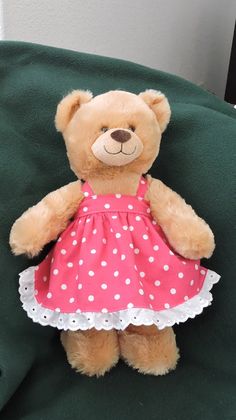 a brown teddy bear wearing a pink and white polka dot dress sitting on a green chair