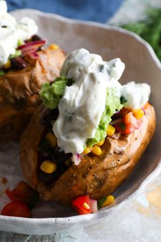 two loaded baked potatoes in a bowl with sour cream on top