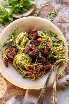 a white bowl filled with pasta and meat on top of a table next to silverware