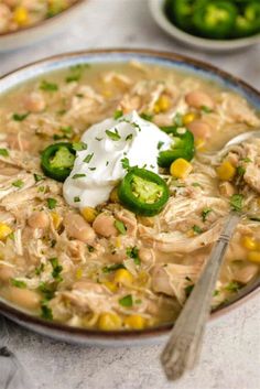 a bowl of chicken and bean soup with sour cream on top, next to two bowls of jalapenos