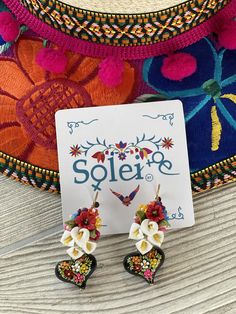 These beautiful Mexican Artisanal earrings are the perfect accessory to give that feminine touch to your outfit! -The flowers are handmade out of Cold porcelain clay. -The hearts are hand painted on wood: The black lacquer is created by mixing in layers of dirt with a grease from the Cochinilla bug. The flowers are painted on with our finger tips using ground up natural pigments and linseed oil. To finish the process we apply a protective coat to conserve the painting and give it a shiny look. E Whimsical Flower-shaped Handmade Earrings, Artistic Flower-shaped Earrings For Gifts, Whimsical Handmade Flower Earrings For Gift, Bohemian Hand Painted Flower Earrings, Whimsical Handmade Flower Earrings, Artisan Flower Earrings, Artisan Flower Earrings As Gift, Multicolor Flower Polymer Clay Earrings, Multicolor 3d Flower Earrings For Gift