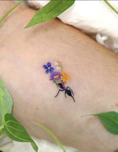 a small tattoo with flowers on the back of someone's left arm, and green leaves surrounding it