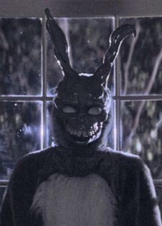 a person wearing a bunny mask and standing in front of a window with an evil look on their face