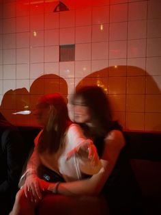 two people sitting on a couch in a room with tile walls and red light coming through the window