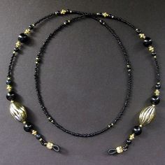 "Inky black beads make up the color of this eyeglass chain (or badge lanyard) when combined with the warm shine of gold plated accents including two large swirl textured egg shape beads. All together creating a beautiful and classy style for this handmade eyeglass chain, face mask holder, or badge lanyard. The length of the strand is made with smooth beads at the nape for the comfort of the wearer and decorative beads at the ends to show off a sense of style. 29.5\" from tip to tip - 75 cm Lengt Black Adjustable Glasses Chain For Parties, Black Glass Glasses Chain For Parties, Black Glass Beaded Necklaces With Beaded Chain, Black Glass Beaded Necklace With Beaded Chain, Adjustable Black Glasses Chains For Parties, Elegant Black Glasses Chains For Party, Black Beaded Glasses Chains As Fashion Accessory, Black Glass Beaded Necklace, Black Beaded Glasses Chains For Fashion