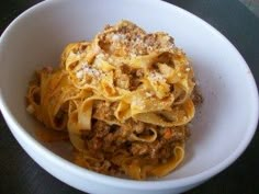 a white bowl filled with pasta and meat on top of a black table next to a fork