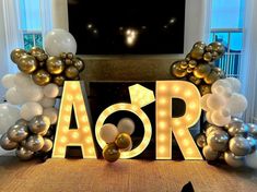 the letters are made out of balloons and gold foil balls in front of a fireplace