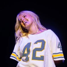 a woman in a football jersey laughing and holding a cell phone up to her ear