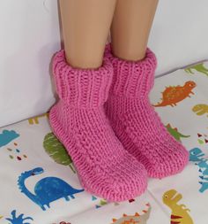 a doll's legs wearing pink knitted socks with dinosaurs on the floor next to it