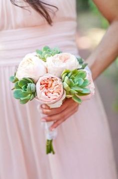 a woman in a pink dress holding a bouquet of roses and succulents