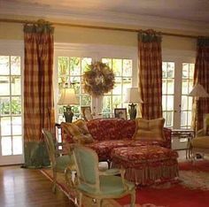 a living room filled with lots of furniture next to two large windows covered in curtains