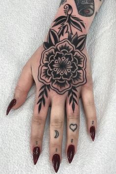 a woman's hand with black and white tattoos on her left arm, holding a flower