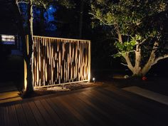 a wooden fence lit up at night with lights on the ground and trees in the background