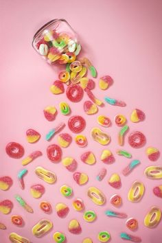 colorful candies spilling out of a glass jar on pink background stock - fotop