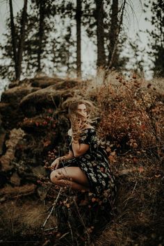 a woman is sitting in the woods with her hands on her face and looking at something