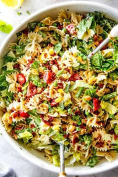 a white bowl filled with pasta salad next to lemon wedges and utensils