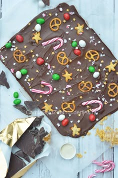 a chocolate cake decorated with christmas decorations and candies on a white wooden table next to gold foil