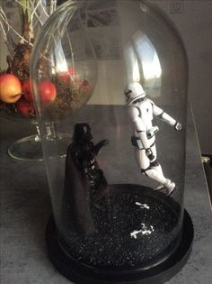 star wars figurines are under a glass dome on a table with fruit in the background