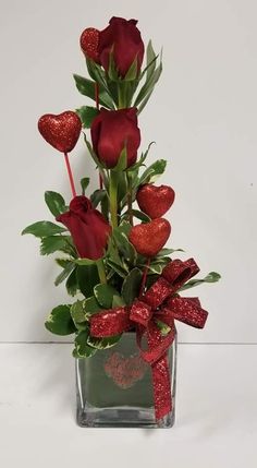 a vase filled with red roses and greenery