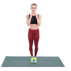 a woman standing on a yoga mat with her hands behind her head and looking at the camera