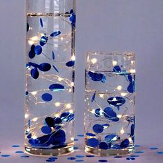 two vases with blue flowers and lights in them