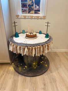 a cake is sitting on top of a wooden table with lights around it in front of a window