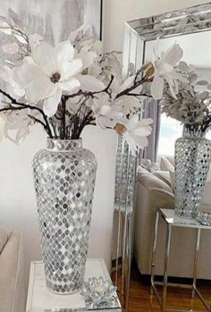 two silver vases with flowers in them sitting on a table next to a mirror