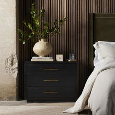 a bed with white sheets and pillows next to a black night stand with a potted plant on top