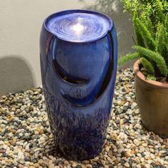 a blue vase sitting on top of a gravel ground next to a potted plant