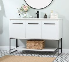 a bathroom vanity with a round mirror above it and a basket on the floor next to it